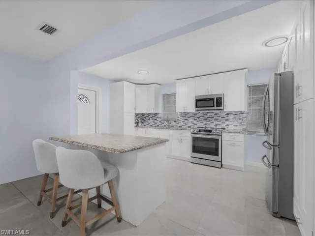 Kitchen featuring stainless steel appliances, white cabinetry, a center island, decorative backsplash, and recessed lighting