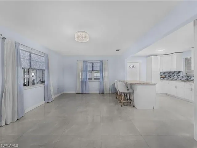 Kitchen with a kitchen breakfast bar, white cabinetry, decorative backsplash, light stone counters, and a center island
