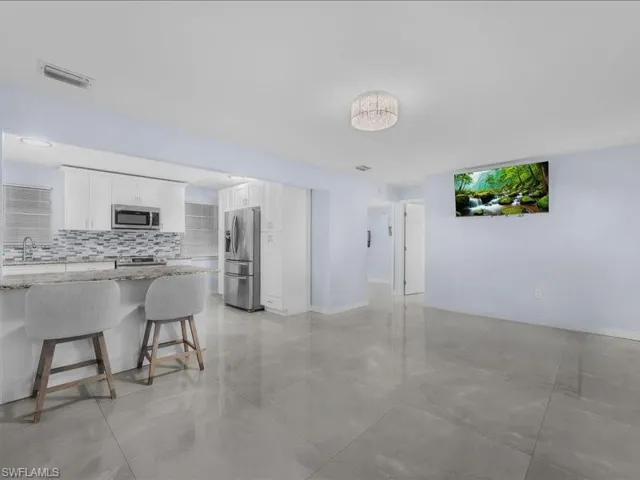 Kitchen with light stone countertops, white cabinets, a breakfast bar, tasteful backsplash, and stainless steel appliances