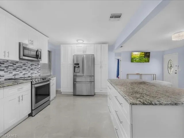 Kitchen featuring stainless steel appliances, white cabinets, light stone counters, and tasteful backsplash