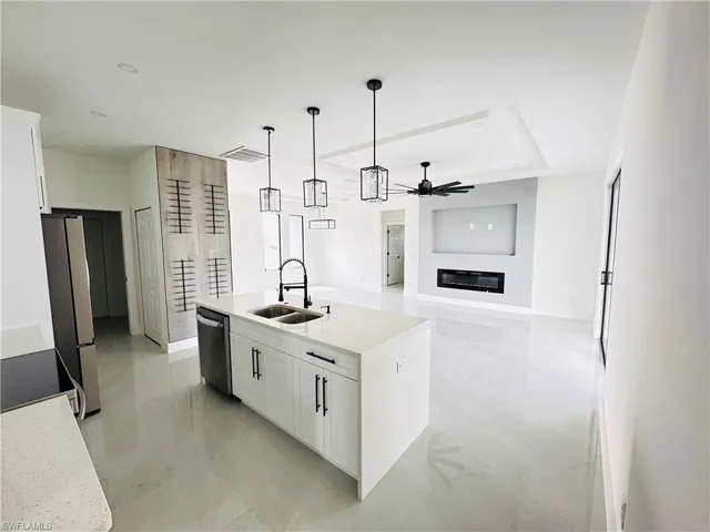 Kitchen featuring stainless steel appliances, hanging light fixtures, white cabinetry, a sink, and an island with sink