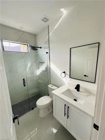 Full bathroom featuring toilet, vanity, visible vents, marble finish floor, and a marble finish shower