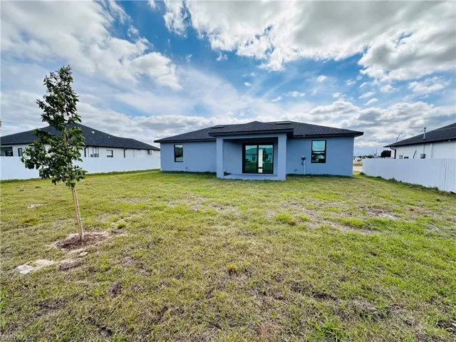 Rear view of house with stucco siding, fence, and a yard