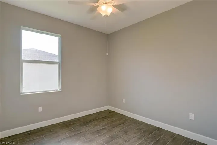 Unfurnished room with a ceiling fan, wood finish floors, and baseboards