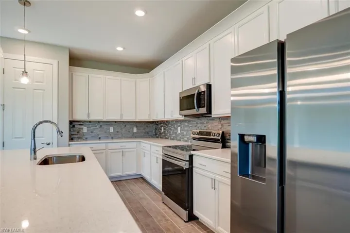 Kitchen featuring appliances with stainless steel finishes, hanging light fixtures, wood tiled floor, white cabinetry, and a sink