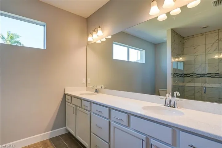 Bathroom featuring baseboards, double vanity, a sink, and a shower stall