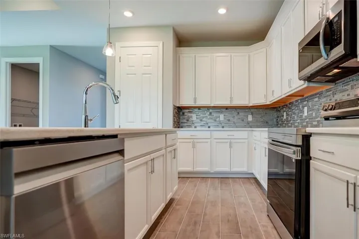 Kitchen featuring white cabinets, hanging light fixtures, appliances with stainless steel finishes, light countertops, and decorative backsplash