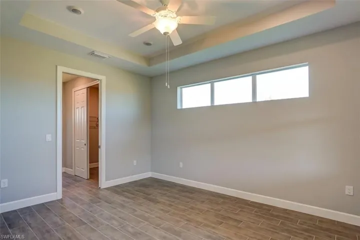 Spare room featuring ceiling fan, wood finished floors, visible vents, baseboards, and a tray ceiling