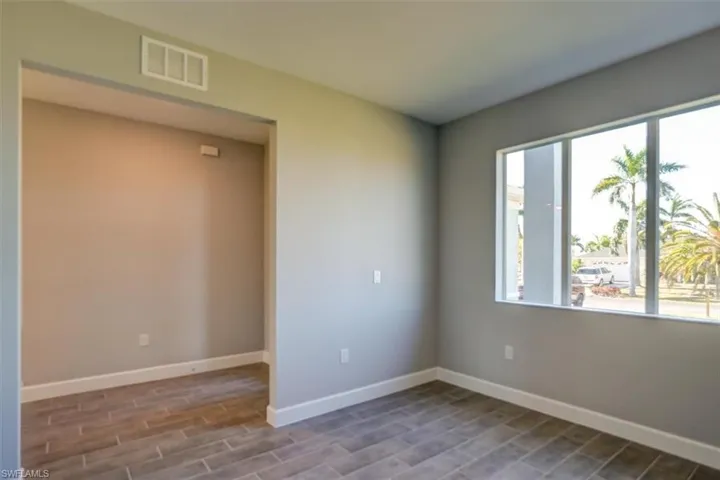 Empty room featuring a wealth of natural light, wood finished floors, visible vents, and baseboards