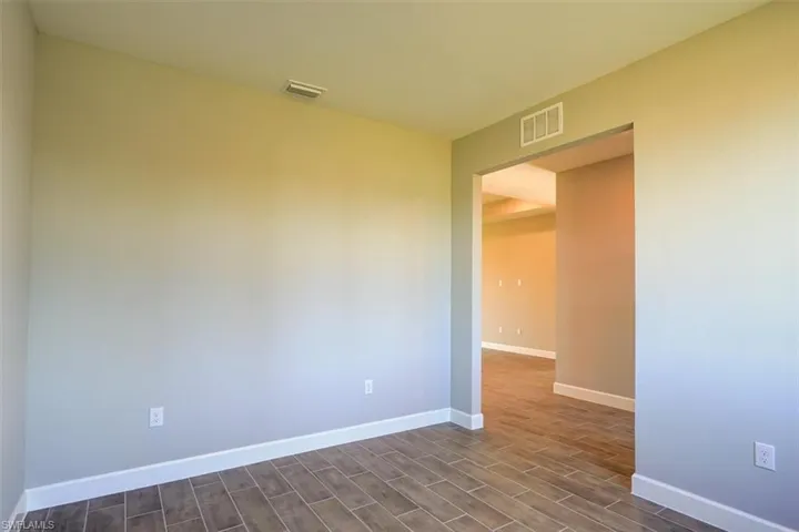 Empty room featuring dark wood-style flooring, visible vents, and baseboards