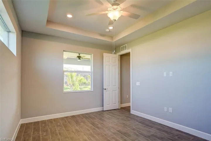 Spare room with recessed lighting, wood finished floors, visible vents, baseboards, and a tray ceiling