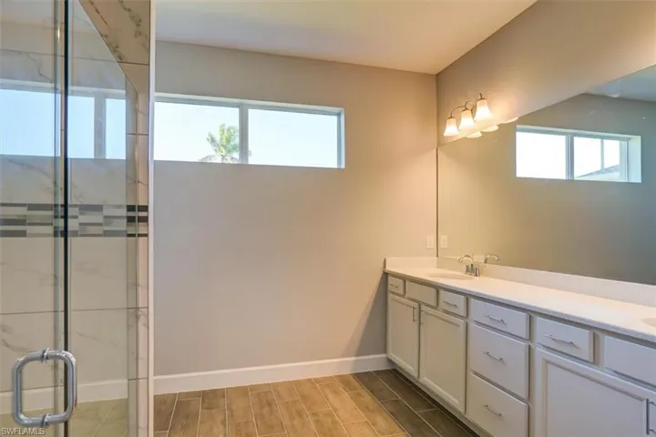 Bathroom with wood finish floors, double vanity, a stall shower, a sink, and baseboards