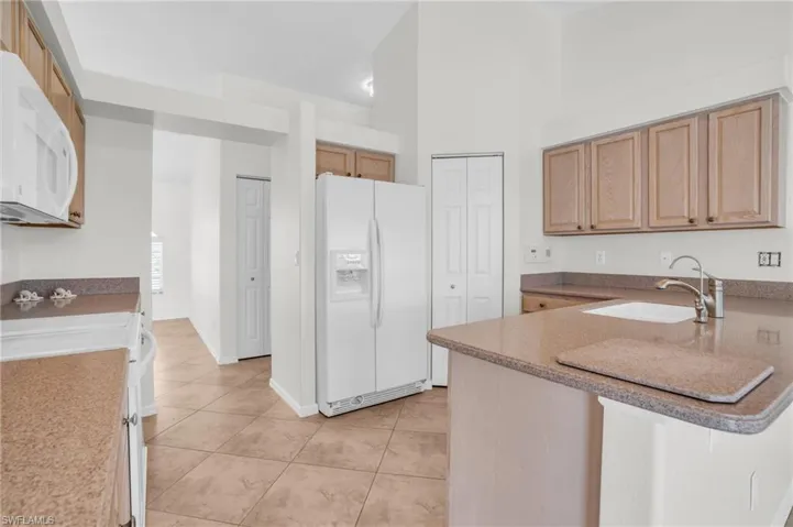 Kitchen featuring sink, kitchen peninsula, white appliances, and light tile patterned floors