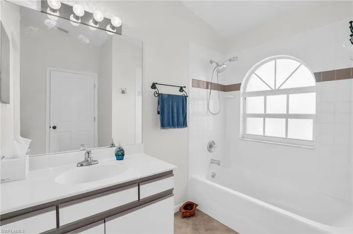 Bathroom with vanity, tiled shower / bath combo, lofted ceiling, and tile patterned floors