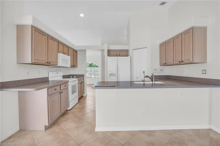 Kitchen featuring light tile floors, white appliances, and sink with counter height seating