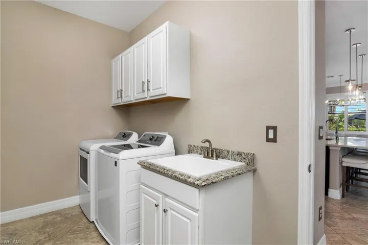 Clothes washing area with separate washer and dryer, sink, light tile flooring, and cabinets