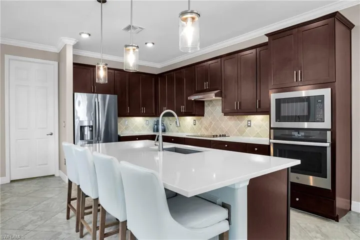 Kitchen with hanging light fixtures, stainless steel appliances, backsplash, sink, and light tile floors