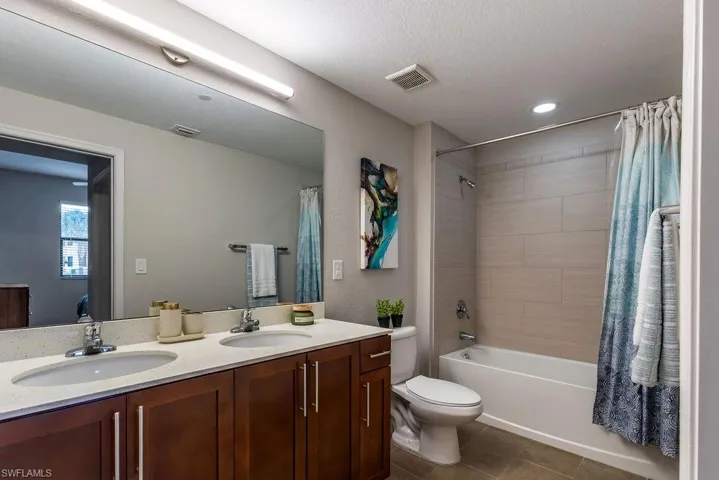 Bathroom featuring shower / bathtub combination with curtain, double vanity, dark tile patterned floors, and recessed lighting