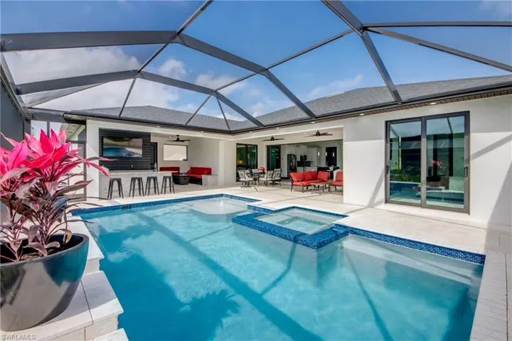 view of outdoor pool, with connected spa, lounge area, outdoor wet bar, and glass enclosures