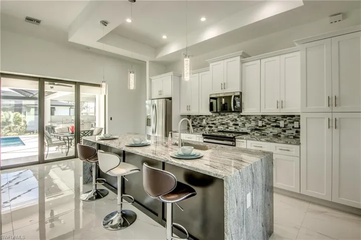 Kitchen with an island featuring a "waterfall" granite top- tasteful backsplash, stainless steel finishes, and marble floord.