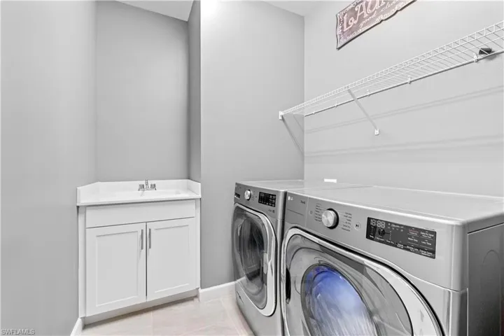 Laundry room featuring light tile patterned floors, a sink, cabinet space, washing machine and clothes dryer, and baseboards