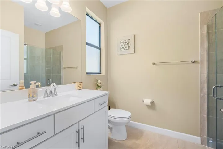 Bathroom featuring toilet, a tile shower, tile patterned floors, baseboards, and vanity