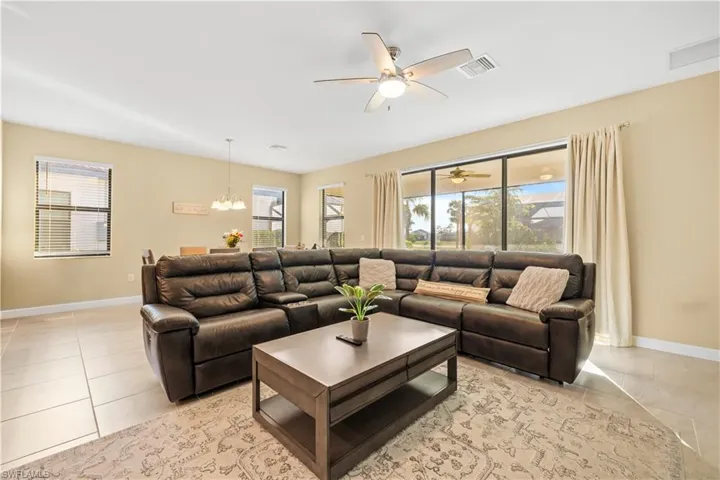 Living room with light tile patterned floors, baseboards, visible vents, and ceiling fan with notable chandelier