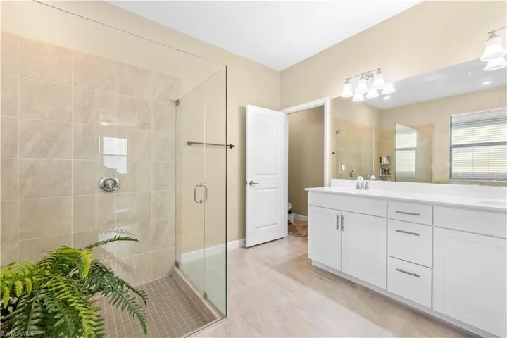 Bathroom with toilet, a sink, a shower stall, tile patterned flooring, and double vanity