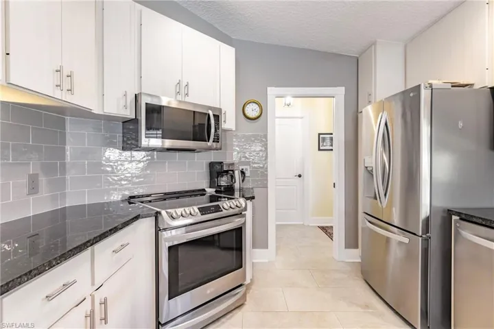 Kitchen featuring dark stone counters, backsplash, light beige cabinetry, appliances with stainless steel finishes, and light tile floors