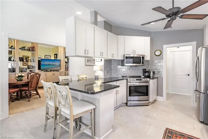 Kitchen with light beige cabinetry, a kitchen breakfast bar, stainless steel appliances, ceiling fan, and and view of den doors open.
