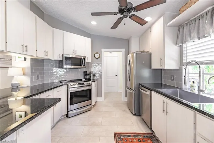 Kitchen featuring stainless steel appliances, backsplash, sink, light tile flooring, and ceiling fan