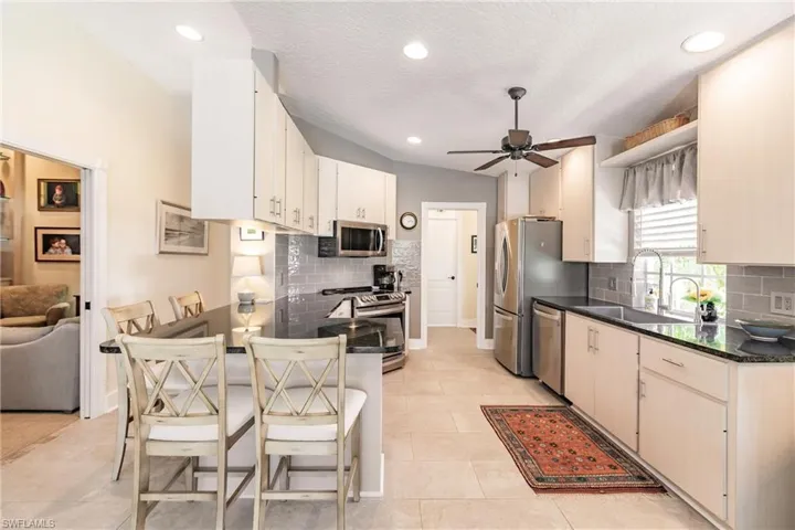 Kitchen with stainless steel appliances, backsplash, sink, ceiling fan, and light tile floors