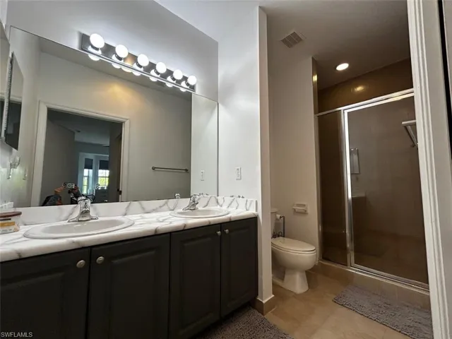 Bathroom featuring double vanity, a shower stall, and light tile patterned floors