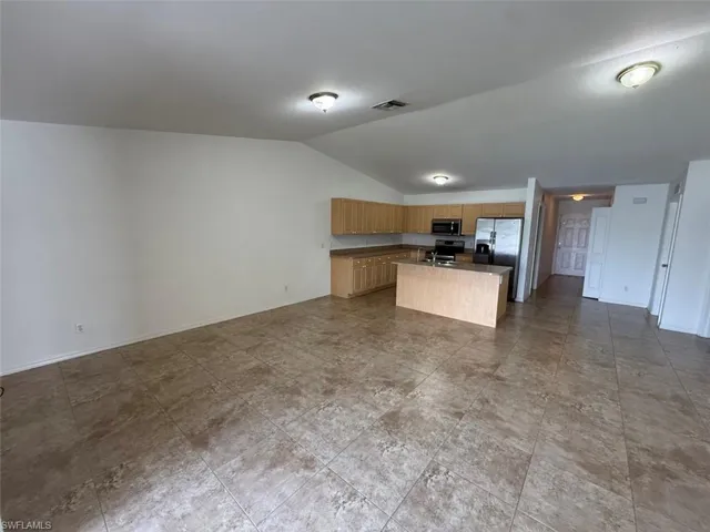 Kitchen with stainless steel appliances, open floor plan, vaulted ceiling, a center island with sink, and dark countertops