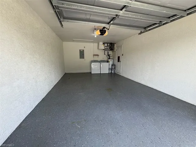 Garage with washing machine and dryer, a textured wall, a garage door opener, water heater, and electric panel