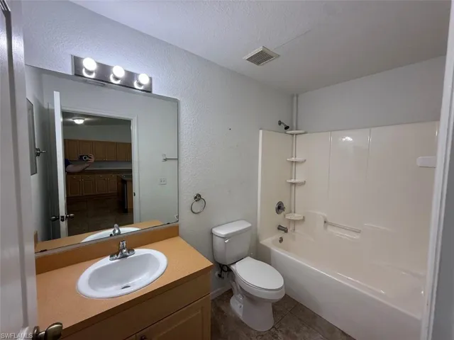 Full bathroom with a textured wall, tile patterned floors, vanity, shower / bath combination, and a textured ceiling