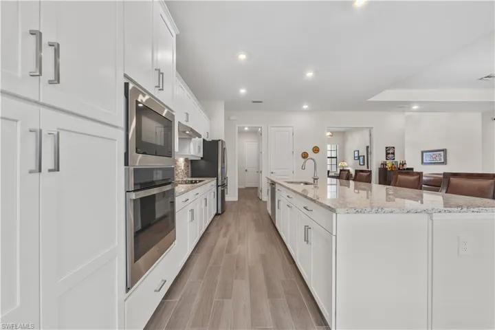 Kitchen featuring white cabinetry, stainless steel appliances, granite countertops, wood-finish flooring, and recessed lighting