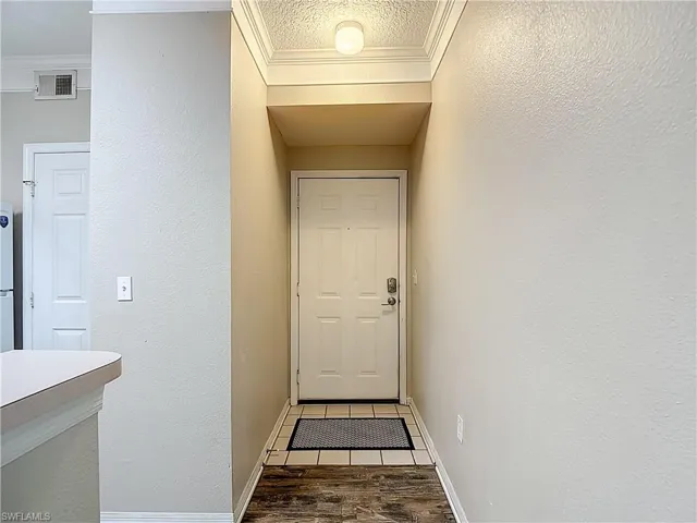 Entryway with a textured wall, wood finished floors, a textured ceiling, and crown molding