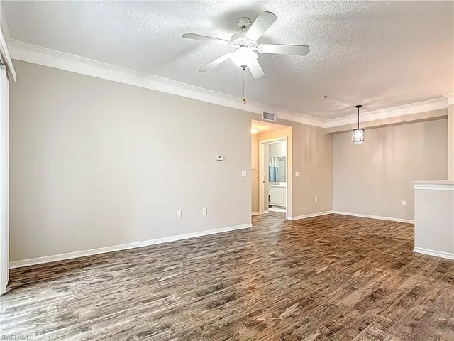 Empty room with a textured ceiling, a ceiling fan, dark wood finished floors, and ornamental molding