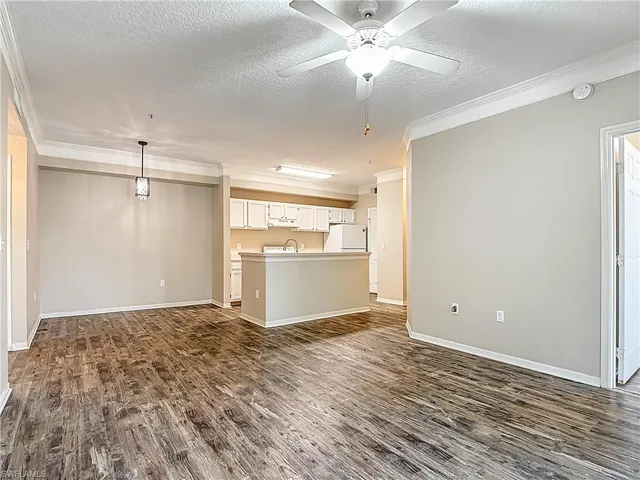 Unfurnished living room with a textured ceiling, dark wood-style floors, ornamental molding, and a ceiling fan