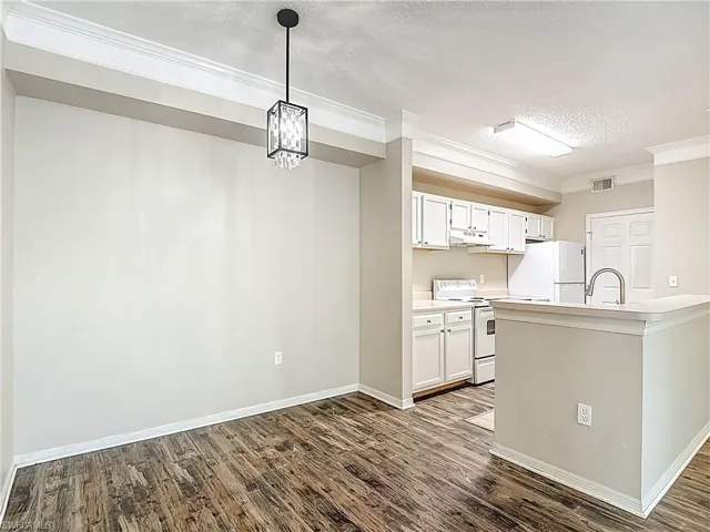 Kitchen featuring light countertops, white appliances, white cabinetry, a textured ceiling, and crown molding
