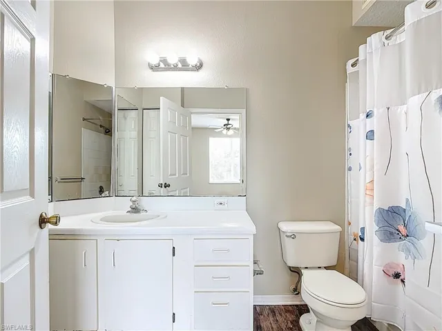 Full bath with vanity, dark wood-type flooring, a textured wall, and a ceiling fan