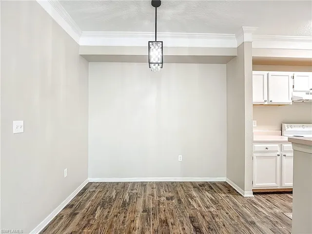 Unfurnished dining area with dark wood-style flooring, a textured ceiling, and ornamental molding