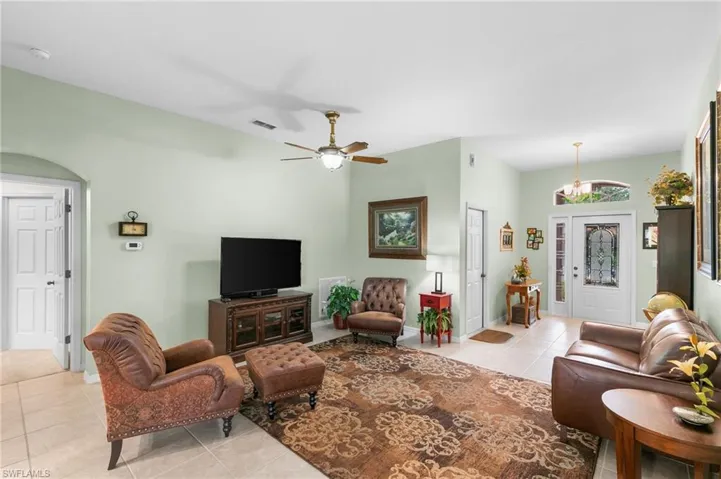 Living room featuring ceiling fan with notable chandelier and light tile floors