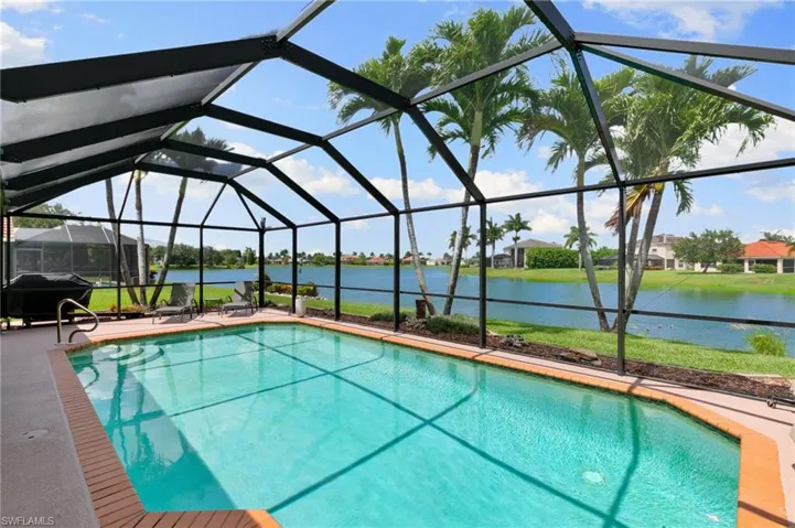 View of swimming pool featuring area for grilling, a patio area, glass enclosure, and a water view