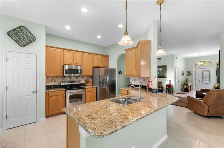 Kitchen with kitchen peninsula, pendant lighting, backsplash, sink, and appliances with stainless steel finishes