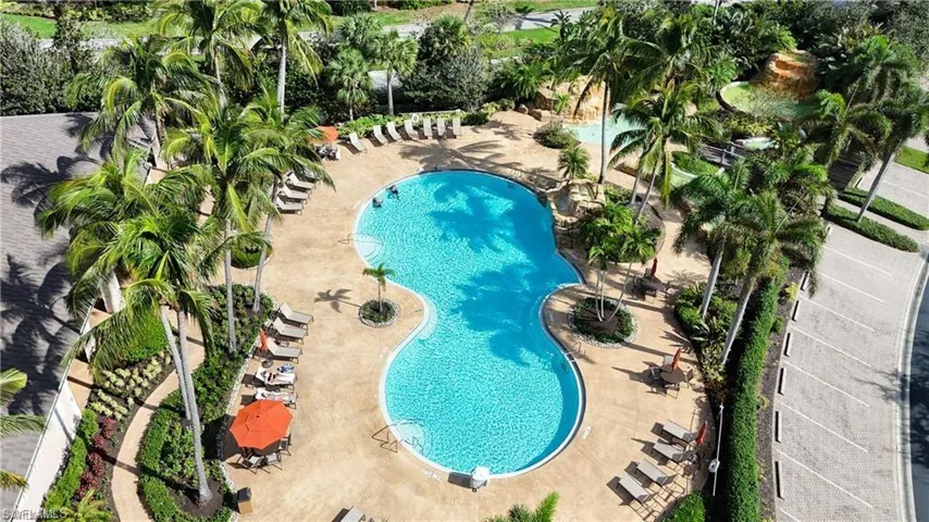 Resort-style pool area featuring a freeform swimming pool, ample lounge seating, and surrounding tropical landscaping