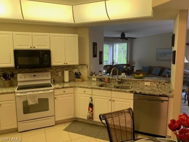 Kitchen with black microwave, electric stove, stainless steel dishwasher, decorative backsplash, and white cabinets