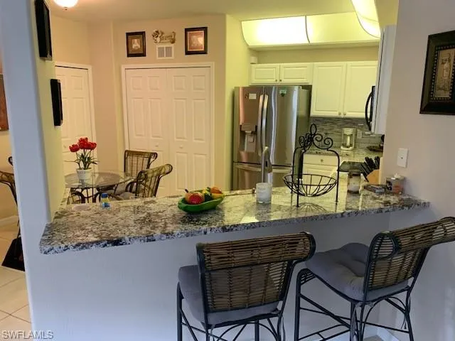 Kitchen with stainless steel refrigerator with ice dispenser, a peninsula, dark stone counters, white cabinets, and light tile patterned floors