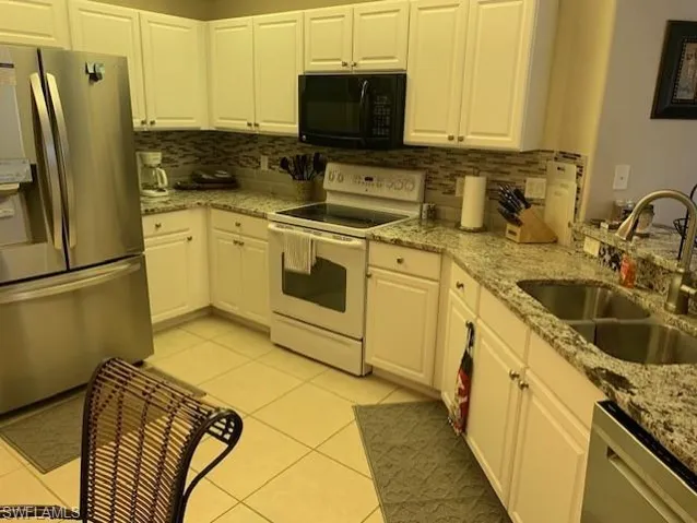 Kitchen featuring appliances with stainless steel finishes, decorative backsplash, white cabinetry, and light tile patterned flooring